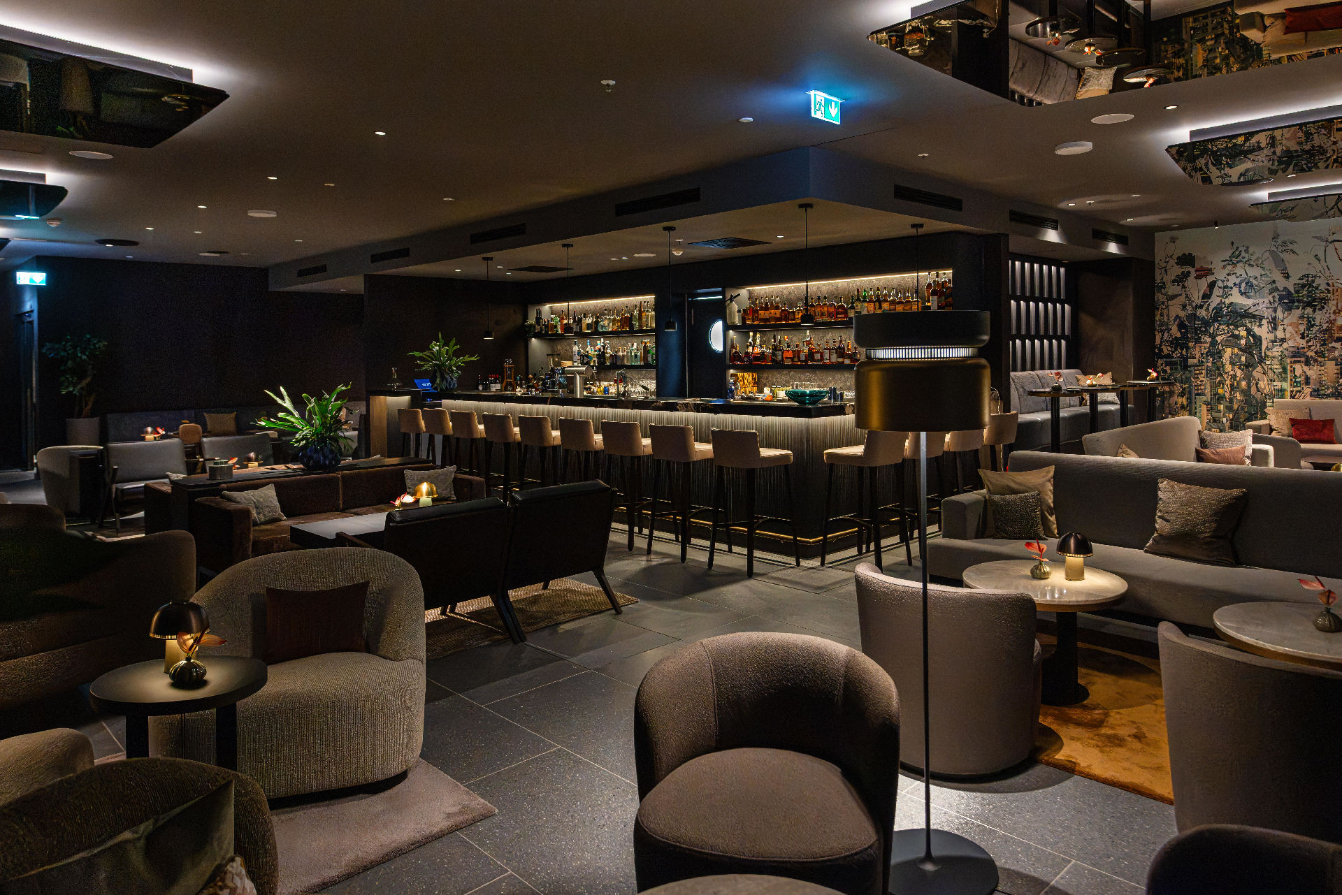 Elegante Hotelbar mit zentraler Bartheke, hohen Barhockern und mehreren gemütlichen Sitzbereichen. Warmes Licht, moderne Möbel und dekorative Pflanzen schaffen eine stilvolle Lounge-Atmosphäre.